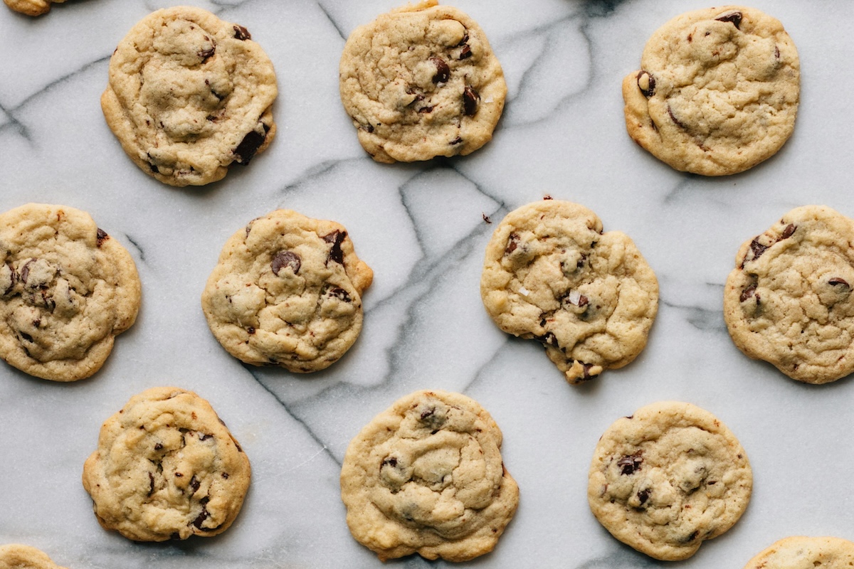 A grid of baked chocolate chip cookies sitting on a marble countertop.