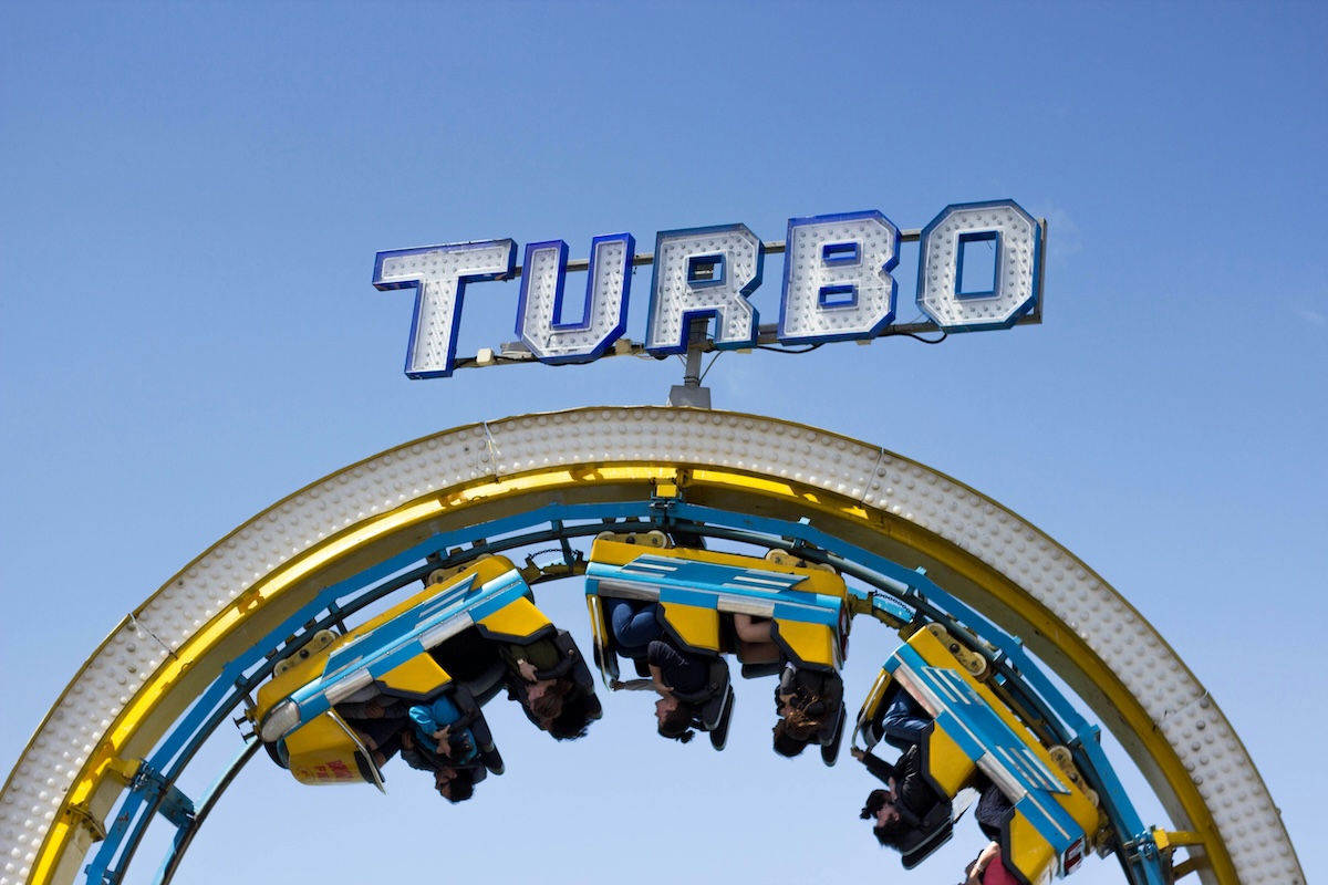 A rollercoaster inversion with passengers mid-rotation. Above the rollercoaster is a large sign that says "Turbo"